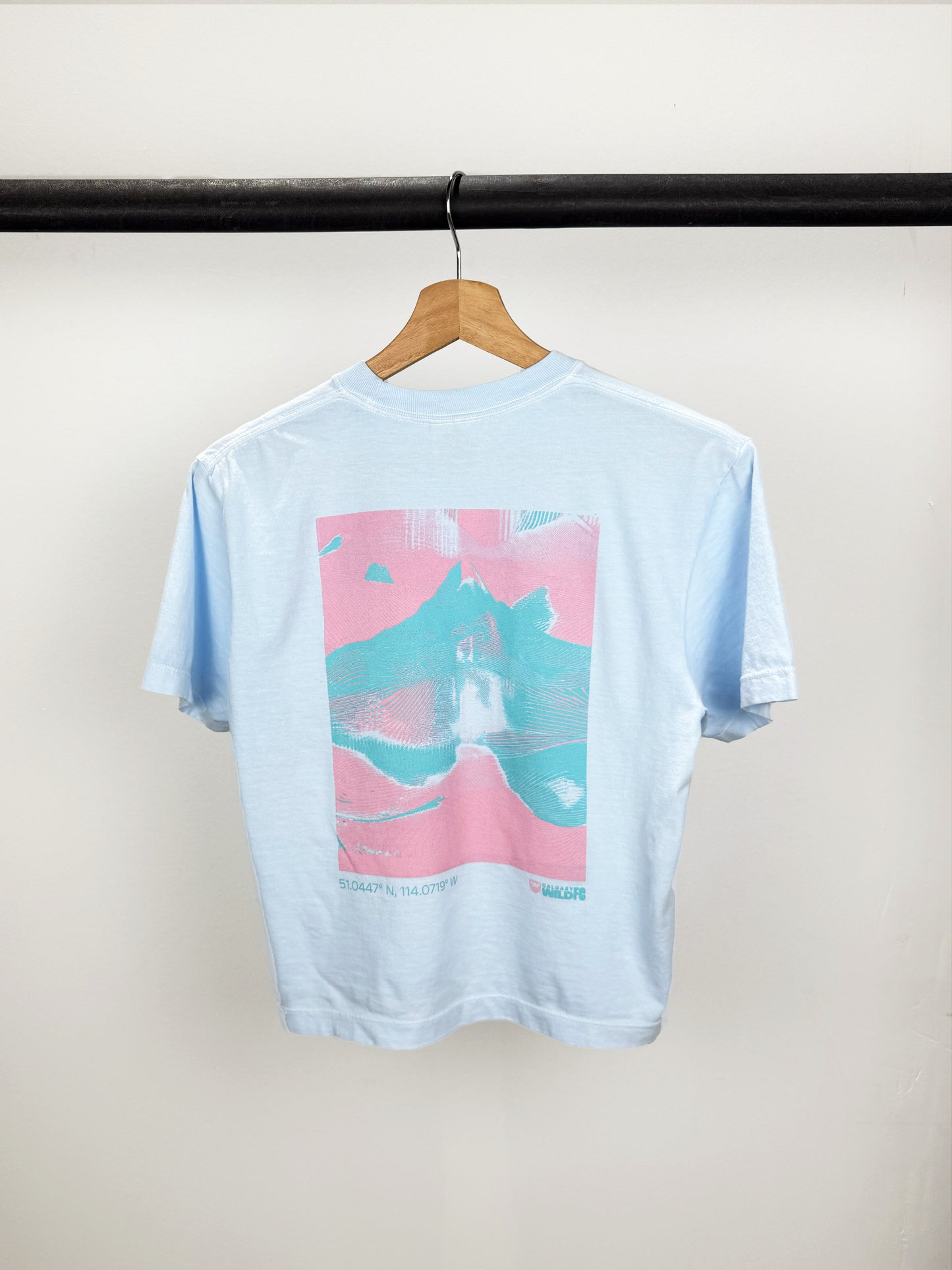 Light blue t-shirt with a colorful graphic on a hanger against a white wall