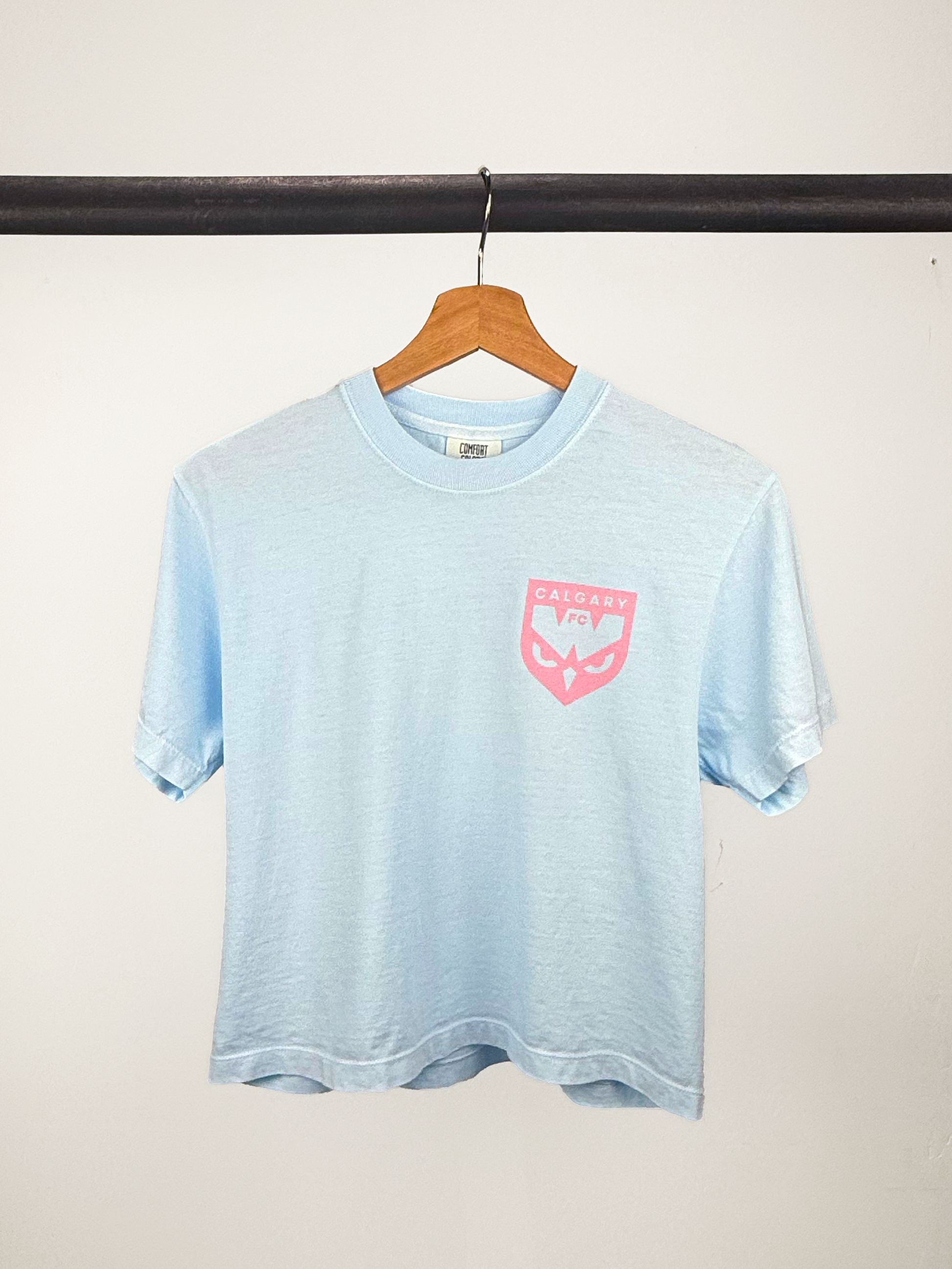 Light blue t-shirt with a pink logo on a hanger against a white background