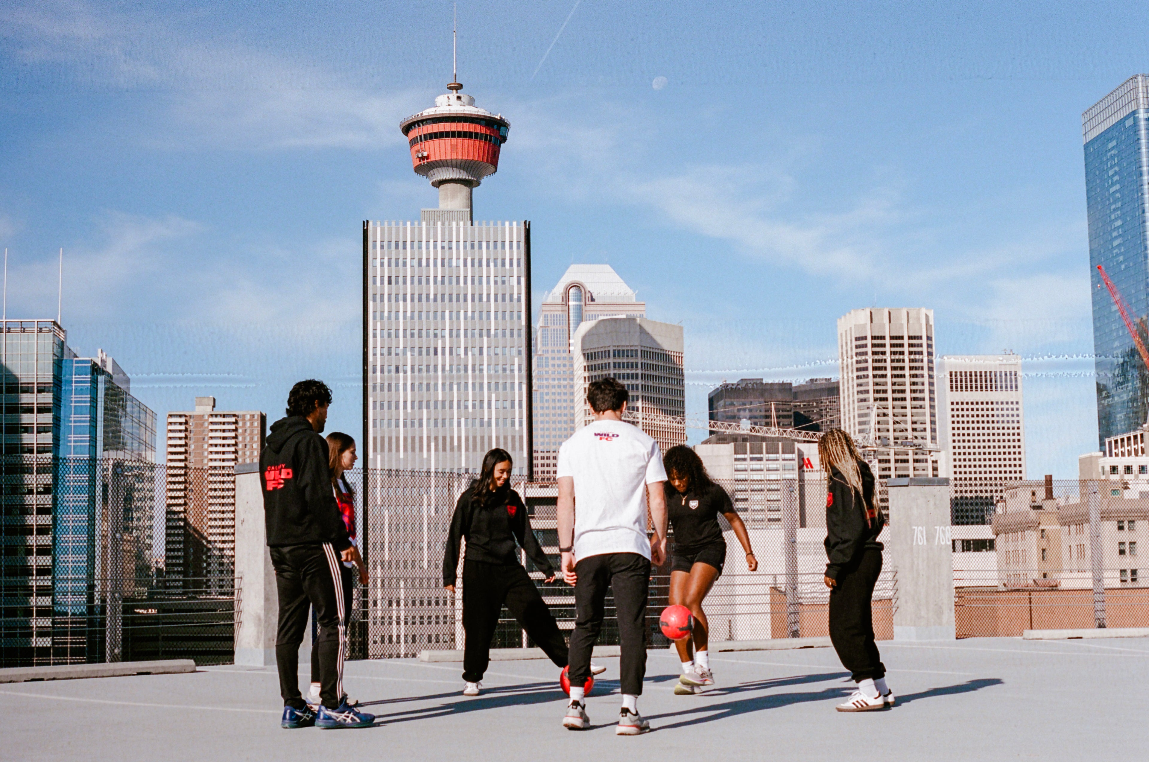 Group of people on a rooftop with a city skyline in the background, including a distinctive tower.